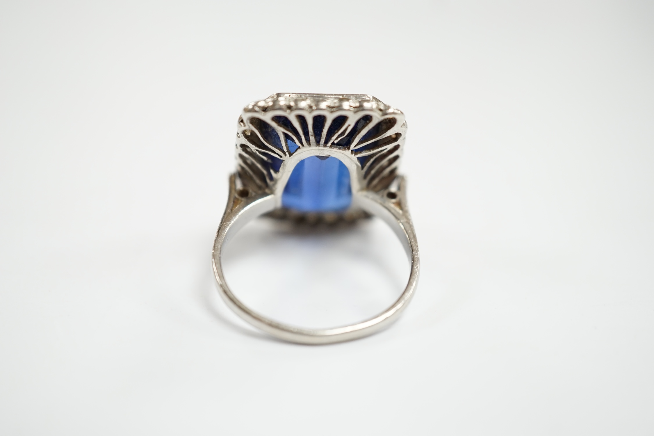 A 1920's white metal and single stone emerald cut synthetic sapphire set dress ring, with millegrain set diamond chip border, size N, gross weight 10 grams.